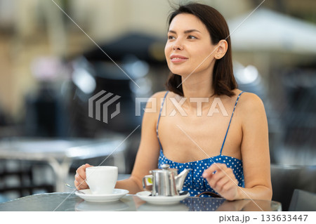 Stylish young brunette woman drinking tea while sitting on terrace of street cafe 133633447