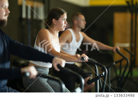 Sportive young girl doing air bike exercises in well-equipped gym 133633498