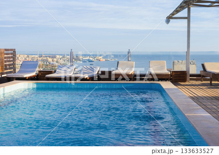 Rooftop pool overlooking cityscape and ocean horizon with loungers Rooftop pool overlooking cityscape and ocean horizon with loungers 133633527