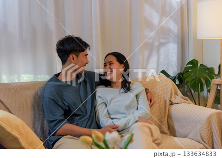 Young happy couple in love at home, woman and man enjoying romantic valentine day together on cozy sofa, smiling cheerfully and embracing, sharing tender loving moments, creating joyful atmosphere. 133634833