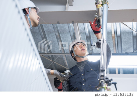 天井が近い高所の足場で単管パイプを固定するクランプなどの施工作業 鳶職や作業員のイメージ 天井が近い高所の足場で単管パイプを固定するクランプなどの施工作業 鳶職や作業員のイメージ 133635138