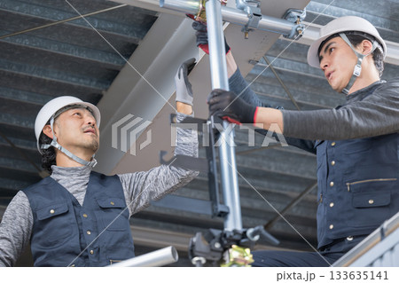 天井が近い高所の足場で単管パイプを固定するクランプなどの施工作業　鳶職や作業員のイメージ　レンチで締 133635141