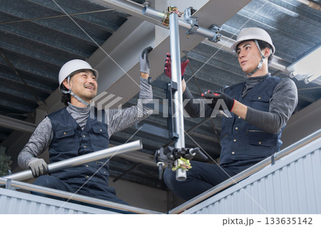 天井が近い高所の足場で単管パイプを固定するクランプなどの施工作業　鳶職や作業員のイメージ　レンチで締 133635142