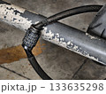 Close-up of a combination cable lock used to secure a motorcycle to a metal bar. Shows worn textures, numbers on the dial, and the sturdy cable, suitable for illustrating security, safety 133635298