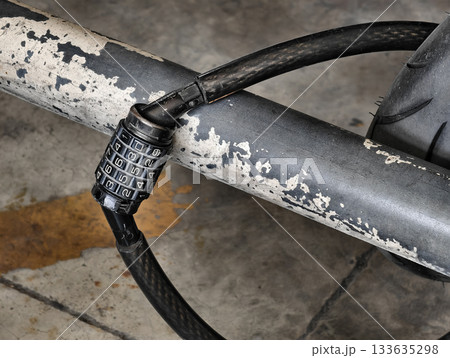 Close-up of a combination cable lock used to secure a motorcycle to a metal bar. Shows worn textures, numbers on the dial, and the sturdy cable, suitable for illustrating security, safety 133635298