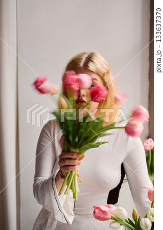 Elegant blonde woman gazing amidst tulip arrangement in studio Elegant blonde woman gazing amidst tulip arrangement in studio 133637370