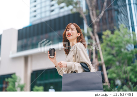Single adult asian business woman holding take away coffee cup and shopping bag on black friday sale 133637481