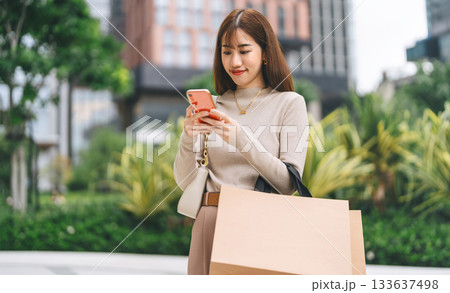Single adult asian woman texting phone holding smartphone and shopping bag city people lifestyle Single adult asian woman texting phone holding smartphone and shopping bag city people lifestyle 133637498