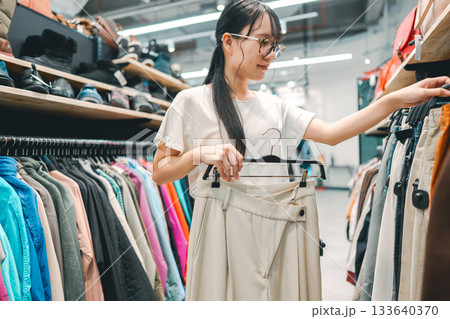 Young adult woman choosing used clothing at second hand clothes shop 133640370