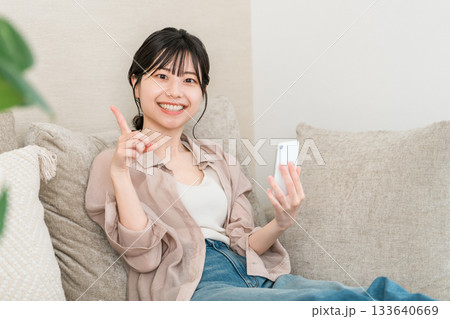 リビングのソファーに座りながらスマホのアプリを使うアジア人女性（紹介,ポイント,おすすめ,案内） 133640669