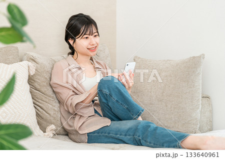 リビングのソファーに座りながらスマホのアプリを使うアジア人女性 133640961