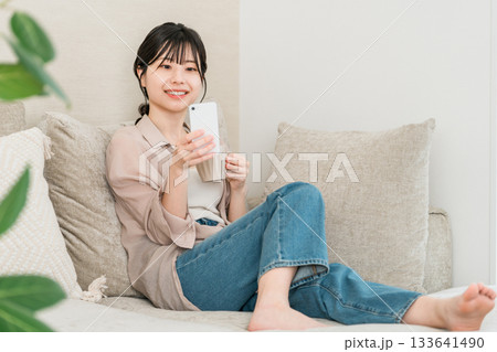 リビングのソファーに座りながらスマホのアプリを使うアジア人女性 リビングのソファーに座りながらスマホのアプリを使うアジア人女性 133641490