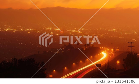 A hazy and dreamy shot of a hilltop with light trails from cars creating a surreal effect against a deep orange sunset 133641506