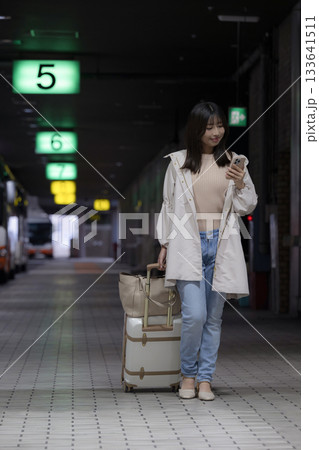 夜の都会の駅、空港やバスターミナルでスマホを見る女性の通勤帰宅シーンと都会のライフスタイル　全身 133641511