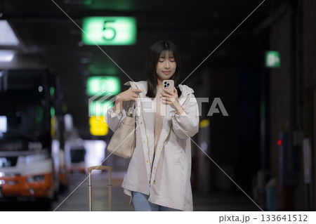 夜の都会の駅、空港やバスターミナルでスマホを見る女性の通勤帰宅シーンと都会のライフスタイル 133641512
