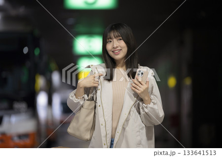 夜の都会の駅やバスターミナルでスマホを持つ女性の通勤帰宅シーンと都会のライフスタイル 133641513