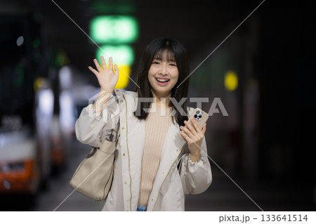 夜の都会の駅や空港、バスターミナルでスマホを見る女性の通勤帰宅シーンと都会のライフスタイル バイバイ 夜の都会の駅や空港、バスターミナルでスマホを見る女性の通勤帰宅シーンと都会のライフスタイル バイバイ 133641514
