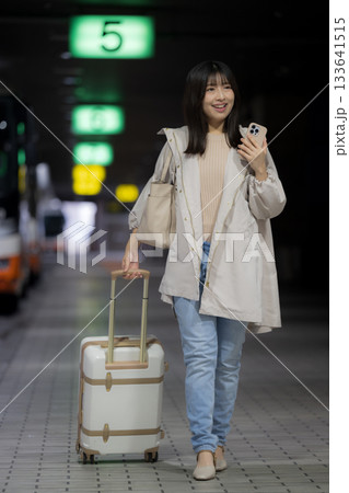 夜の都会の駅、空港やバスターミナルでスマホを見る女性の通勤帰宅シーンと都会のライフスタイル　全身 133641515