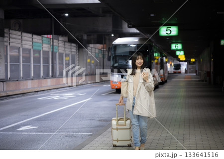 夜の都会の駅、空港やバスターミナルでスマホを見る女性の通勤帰宅シーンと都会のライフスタイル　全身 133641516