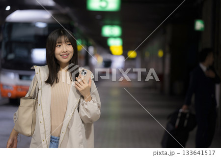 夜の都会の駅やバスターミナルでスマホを見る女性の通勤帰宅シーンと都会のライフスタイル 夜の都会の駅やバスターミナルでスマホを見る女性の通勤帰宅シーンと都会のライフスタイル 133641517