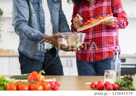 A couple is preparing a fresh salad in the kitchen, with various vegetables on the table. 133641574