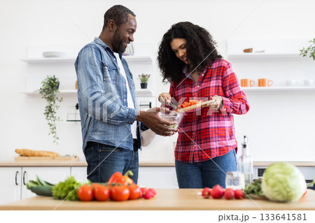 A smiling couple prepares a meal together in a bright, modern kitchen, chopping vegetables. A smiling couple prepares a meal together in a bright, modern kitchen, chopping vegetables. 133641581