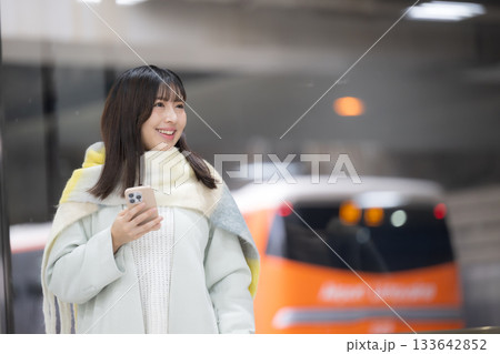 冬の年末年始の帰省、駅のホームやバスターミナルなどでスマホを持つかわいいストールを巻いた女性 133642852