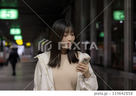 夜の都会の駅や空港、バスターミナルでスマホを見る女性の通勤帰宅シーンと都会のライフスタイル 夜の都会の駅や空港、バスターミナルでスマホを見る女性の通勤帰宅シーンと都会のライフスタイル 133642858