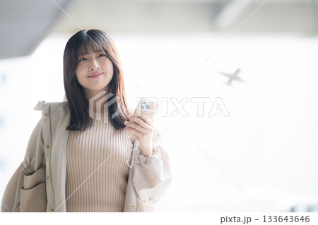 飛行機が背景に見える空港や交通機関のターミナルででスマホを持つ女性の写真 133643646