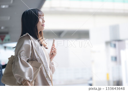 空港や交通機関のターミナルででスマホを持つ女性の写真 旅行や休日のイメージ横顔 空港や交通機関のターミナルででスマホを持つ女性の写真 旅行や休日のイメージ横顔 133643648