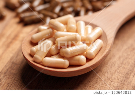 Different vitamin pills placed in wooden spoon and scattered on brown plank board close up 133643812