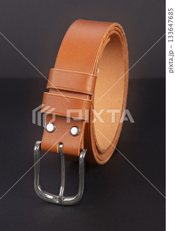 Brown leather belt with metal buckles on a dark gray background. 133647685
