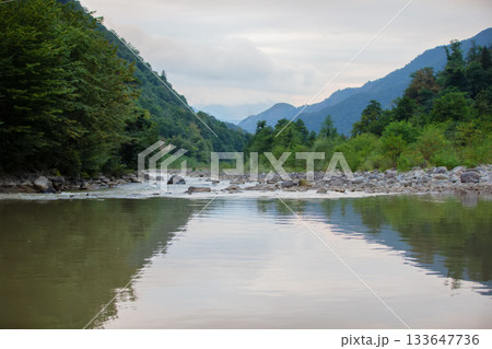 The calm water of the lake against the backdrop of the forested mountains of Georgia. The calm water of the lake against the backdrop of the forested mountains of Georgia. 133647736