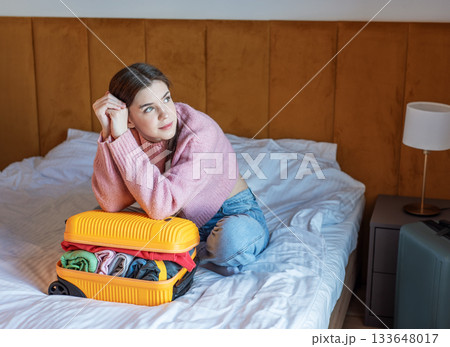 Woman dreaming about travel while packing suitcase on bed 133648017
