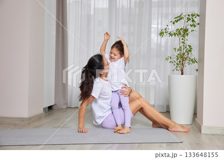 Mother and daughter smiling while exercising and playing on a yoga mat 133648155