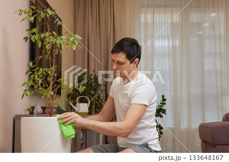 Man cleaning houseplant pot with a rag, performing domestic chores and plant care 133648167