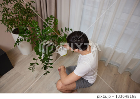 Male person pouring water from a watering can onto indoor houseplants 133648168