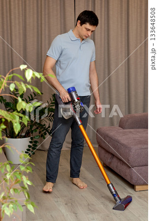 Man cleaning living room floor with a cordless vacuum cleaner 133648508