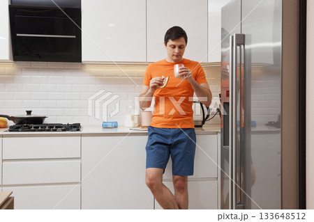Young man standing in a modern kitchen, eating a sandwich and drinking milk Young man standing in a modern kitchen, eating a sandwich and drinking milk 133648512