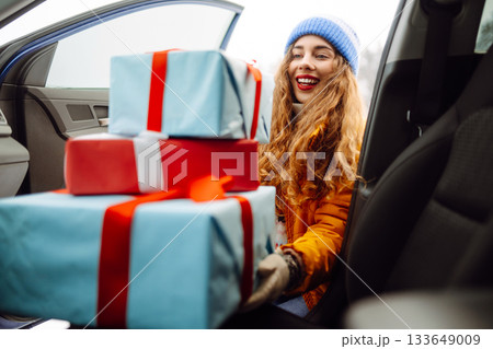 Happy young woman putting New Year's gifts into a car. The eve of the winter holidays, preparation. 133649009