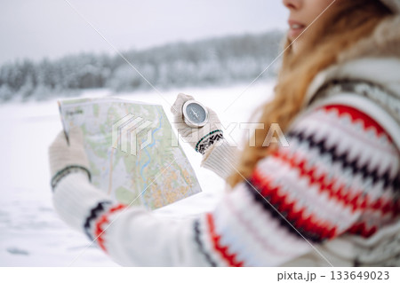 Curly-haired young woman standing in the wild with a map and compass in a snowy forest. Curly-haired young woman standing in the wild with a map and compass in a snowy forest. 133649023