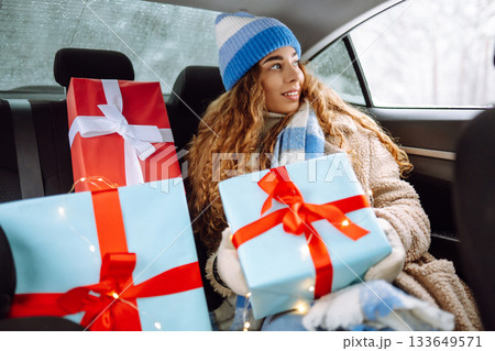 Beautiful young woman with New Year's gifts is riding in back seat of car. Concept of winter holiday 133649571