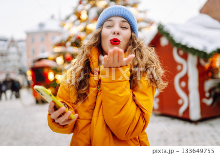 A young woman with curly hair uses a smartphone at a Christmas fair. Vacation concept. 133649755