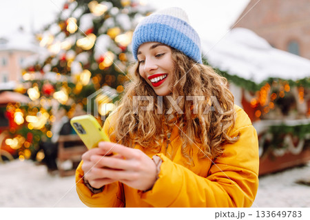 A young woman with curly hair uses a smartphone at a Christmas fair. Vacation concept. A young woman with curly hair uses a smartphone at a Christmas fair. Vacation concept. 133649783