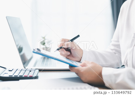 A businesswoman reviews financial report while holding documents and pointing with pen at office desk. Concept of accounting, budget management, financial analysis and corporate business planning. 133649792