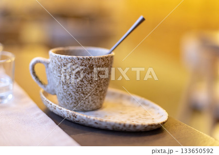 Rustic ceramic coffee cup with spoon on matching saucer in cozy setting Rustic ceramic coffee cup with spoon on matching saucer in cozy setting 133650592