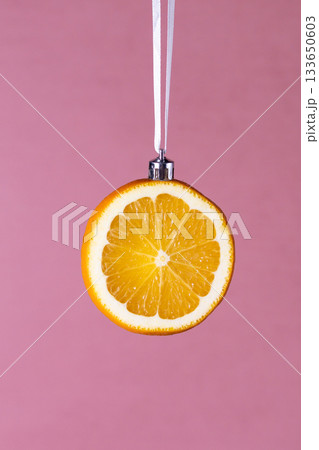 Creative orange slice ornament hanging on pink background Creative orange slice ornament hanging on pink background 133650603