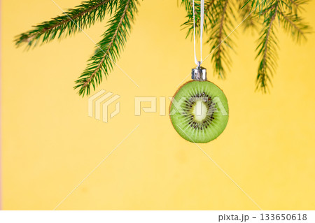 Creative christmas ornament: kiwi slice hanging on pine branch for unique holiday decor Creative christmas ornament: kiwi slice hanging on pine branch for unique holiday decor 133650618