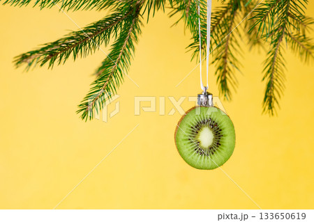 Creative christmas ornament: kiwi slice hanging on pine branch for unique holiday decor Creative christmas ornament: kiwi slice hanging on pine branch for unique holiday decor 133650619