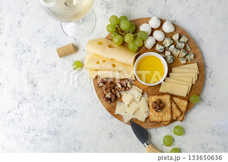 Gourmet cheese platter with grapes, nuts, and honey on rustic wooden board 133650636
